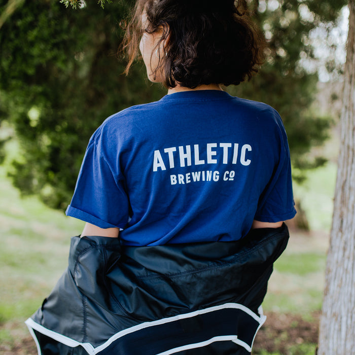 a customer wearing a a navy t-shirt with Athletic Brewing logo in a park
