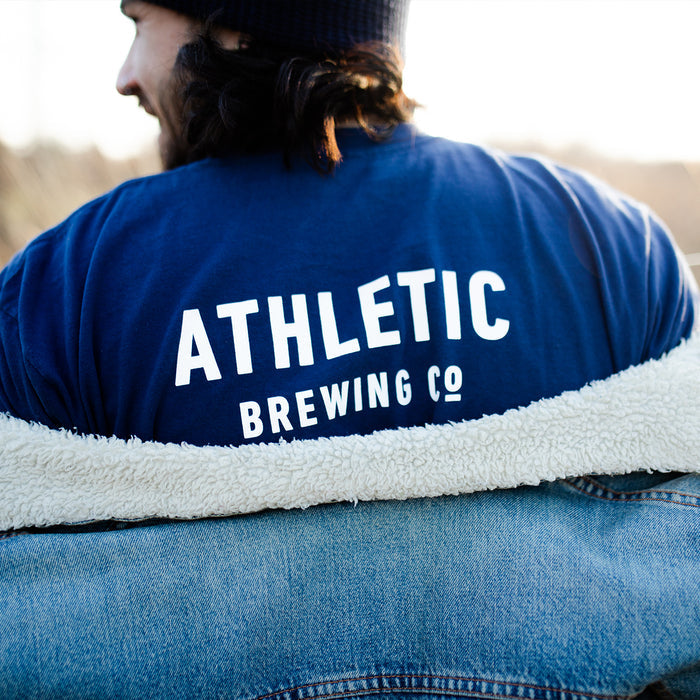 a customer wearing a a navy t-shirt with Athletic Brewing logo in a park