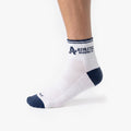 Person wearing white Athletic Brewing quarter crew performance socks with navy toe and heel accents, featuring striped cuffs and Athletic Brewing Co. logo branding near the ankle