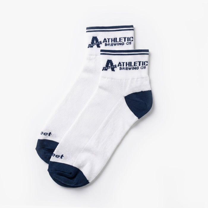 Pair of white Athletic Brewing quarter crew performance socks with navy toe and heel detailing, striped cuffs, breathable mesh knit panels, and Athletic Brewing Co. logo branding.