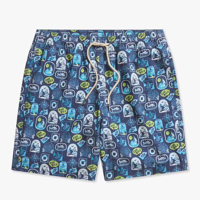 Navy blue swim shorts with an allover coastal-themed print featuring sailboats, seashells, waves, compass designs, Fair Harbor logos, and ‘Run Wild’ graphics in shades of blue, white, and lime green. The shorts have an elastic waistband with a beige drawstring and are shown against a light gray background.