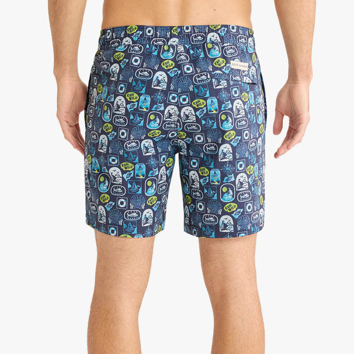 Back view of a person wearing navy blue swim shorts with an allover nautical-inspired print featuring sailboats, shells, and graphic patches. The shorts include a back flap pocket with a small Fair Harbor label.