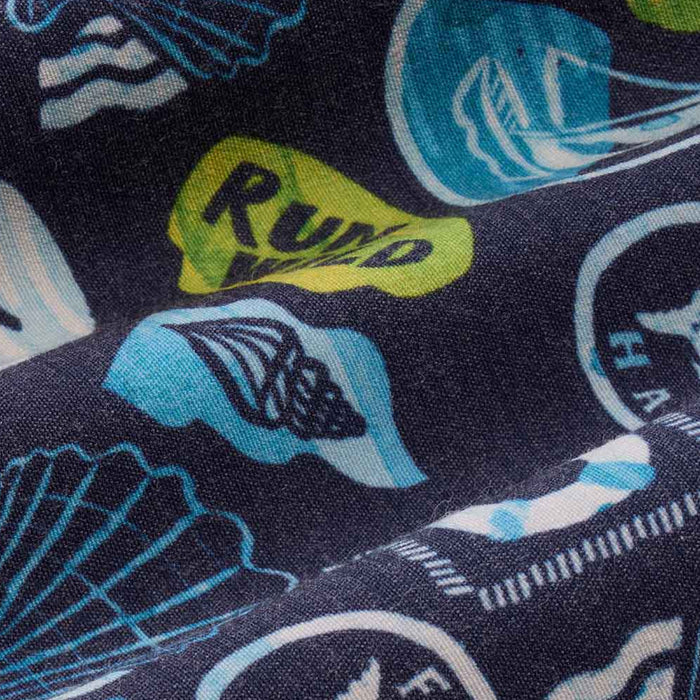 Close-up detail of navy blue fabric with a colorful coastal-themed print featuring sailboats, seashells, and a lime green ‘Run Wild’ graphic.
