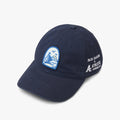 Navy blue baseball cap with a curved brim and embroidered graphics. The front features a blue-and-white patch showing a sailboat on the water with birds flying overhead and a sun near the horizon. The side of the hat includes white embroidered text reading ‘Fair Harbor x Athletic Brewing Co.’ on a light gray background.