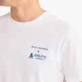 Close-up angled view of a white short-sleeve T-shirt with a blue ‘Fair Harbor x Athletic Brewing Co.’ logo printed on the left chest.
