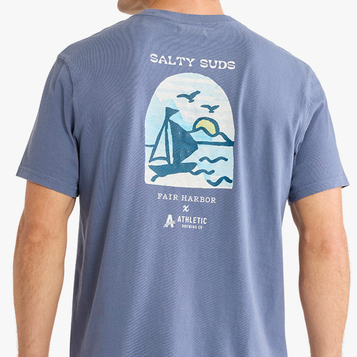 Back view of a faded blue T-shirt featuring a large white and blue sailboat graphic with birds and a sunset scene. Above the graphic is the text ‘Salty Suds,’ and below it reads ‘Fair Harbor x Athletic Brewing Co.