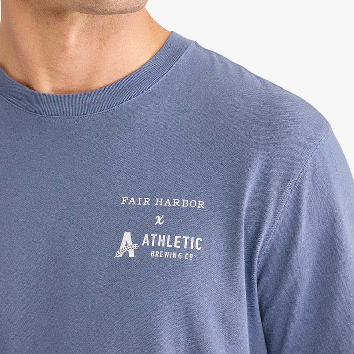 Close-up detail of a faded blue T-shirt showing the white ‘Fair Harbor x Athletic Brewing Co.’ logo printed on the chest.