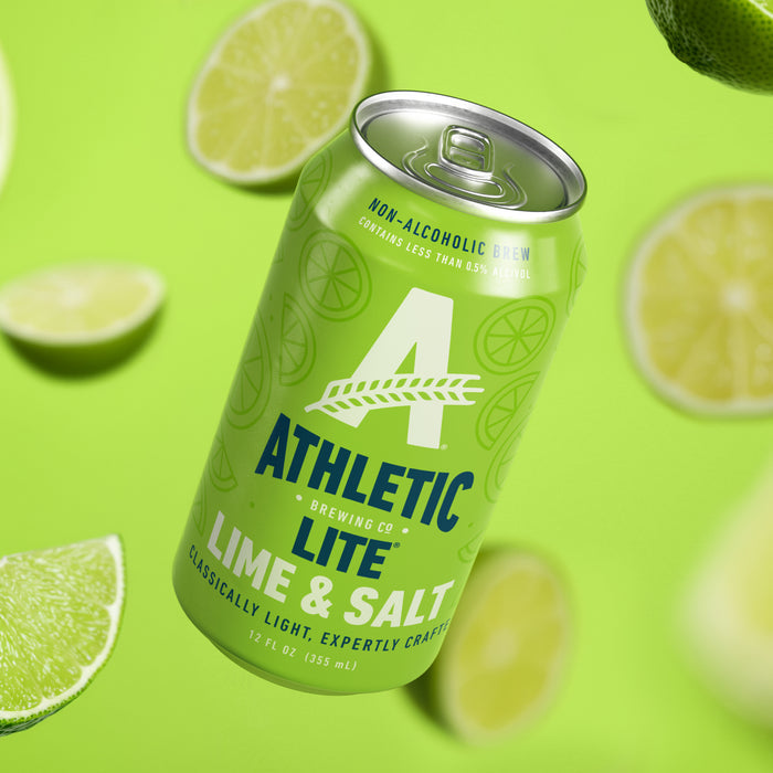 A can of Athletic Lite Lime & Salt non-alcoholic beer floating diagonally against a bright lime green background with scattered lime slices around it.