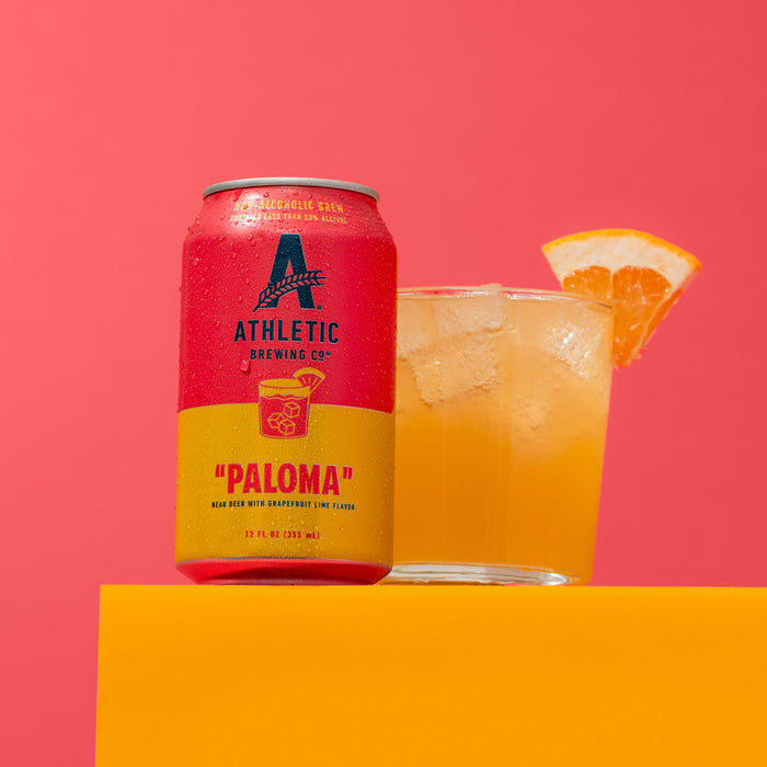 Athletic Brewing Co. cocktail-inspired "Paloma" can with a glass on a pink background