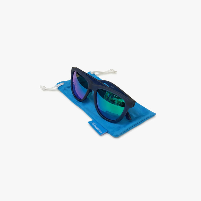 Navy blue sunglasses with mirrored blue-green lenses resting on a bright blue drawstring pouch. The pouch includes a small Knockaround tag, and the product is shown against a light gray background.