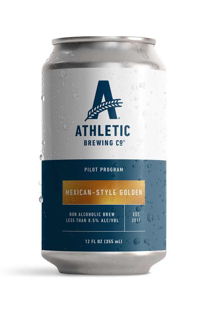 12 fl oz can of Athletic Brewing Pilot Program Mexican-Style Golden non-alcoholic brew with a clean white and navy label accented by a gold nameplate. The can is covered in condensation droplets and features the Athletic Brewing logo, “Pilot Program” branding, and product details including “Less Than 0.5% Alc/Vol.” The can is photographed against a black background, highlighting the limited-release beer packaging.