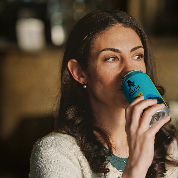 Brunette woman sipping a can of non alcoholic Run Wild Ipa