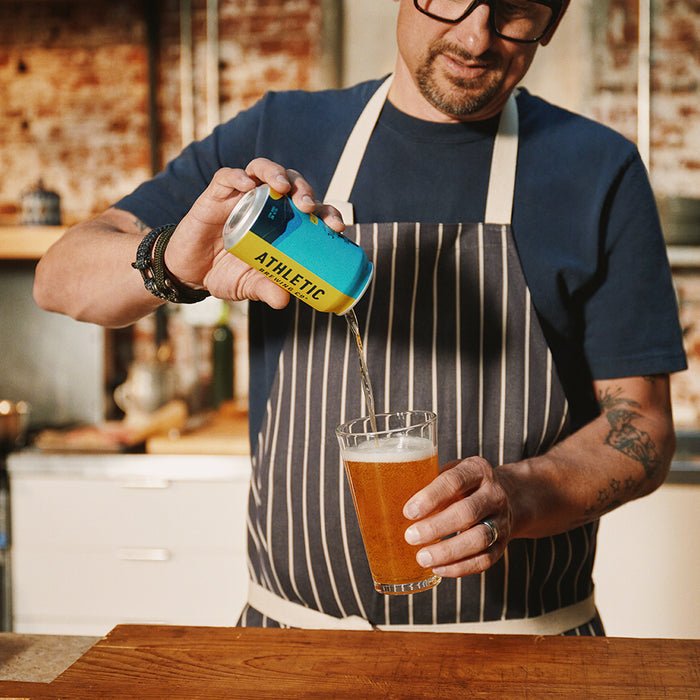 Man wearing a striped apron on top of a navy blue shirt pouring a can of Run Wild Ipa into a pint glass