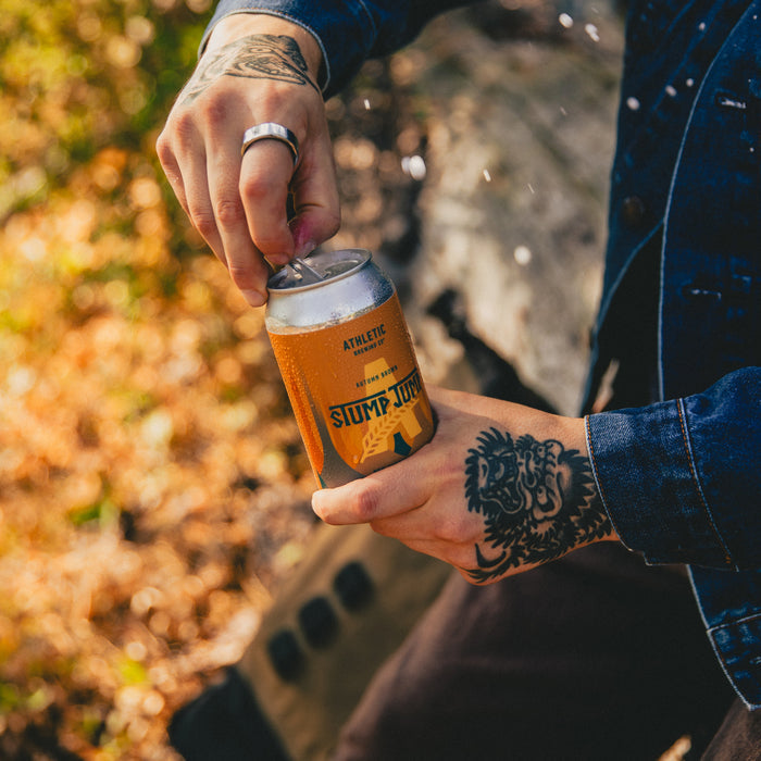 A single can of Stump Jump Non-Alcoholic Brown beer being open by a tattooed man